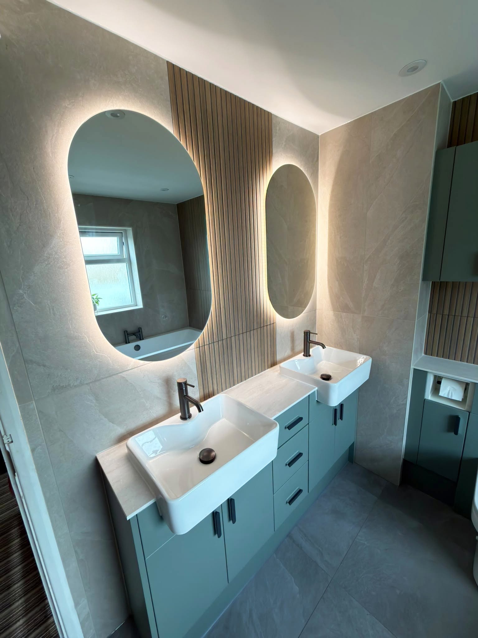 Oval illuminated mirrors above Reed Green basin units with gun metal taps