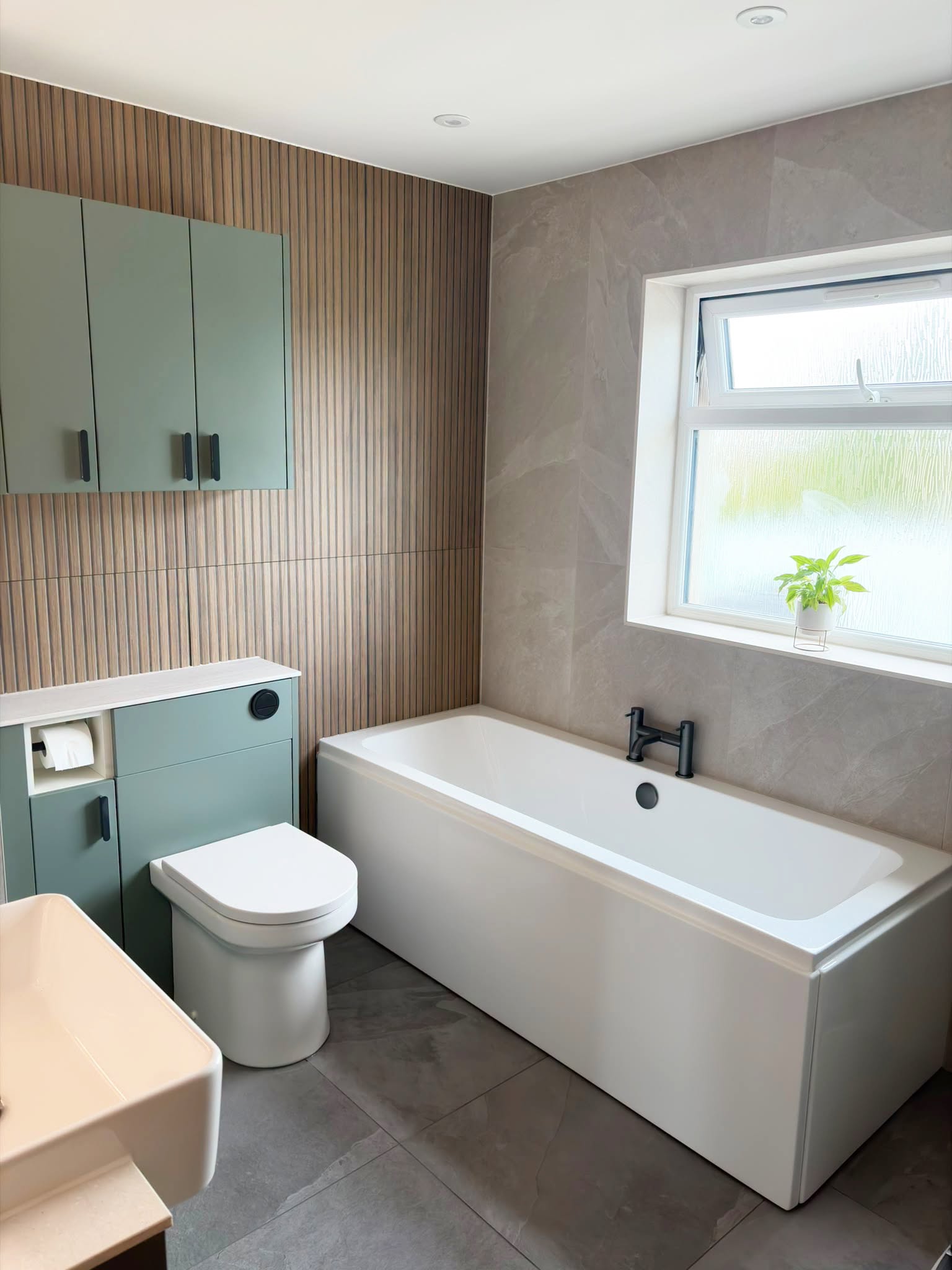 Double-ended bath beneath a window with Reed Green wall cabinets