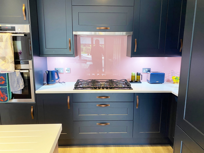 Indigo units with a pink glass splashback and gas hob