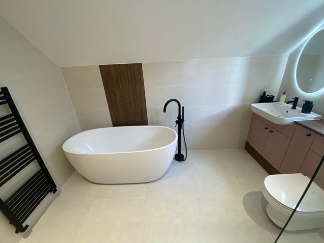 Freestanding bath with a black floor mixer under a sloping ceiling